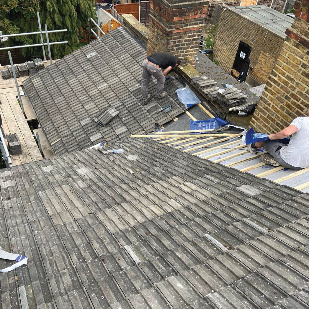 two workers replacig tiles on a roof 