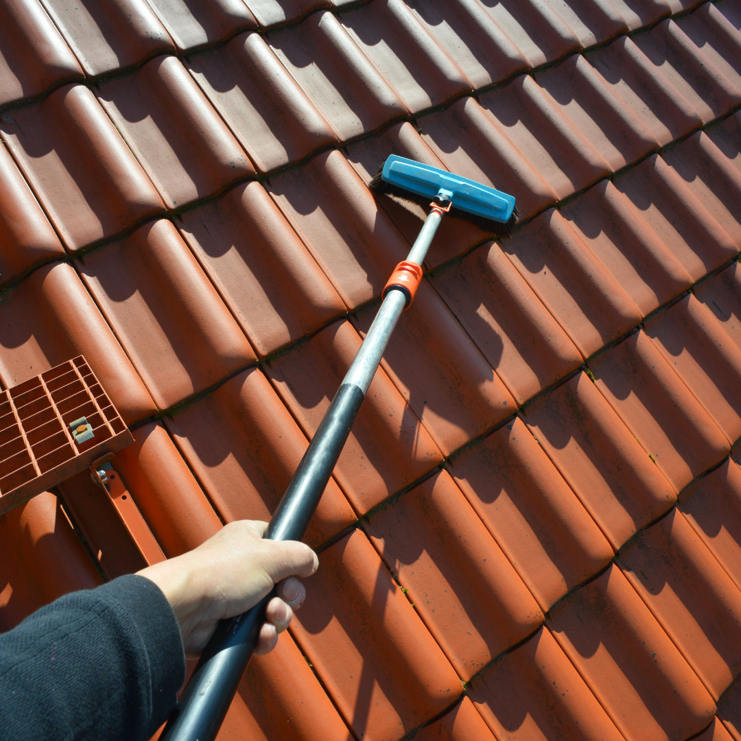 worker with roof cleaning tool on teracotta tiled roof
